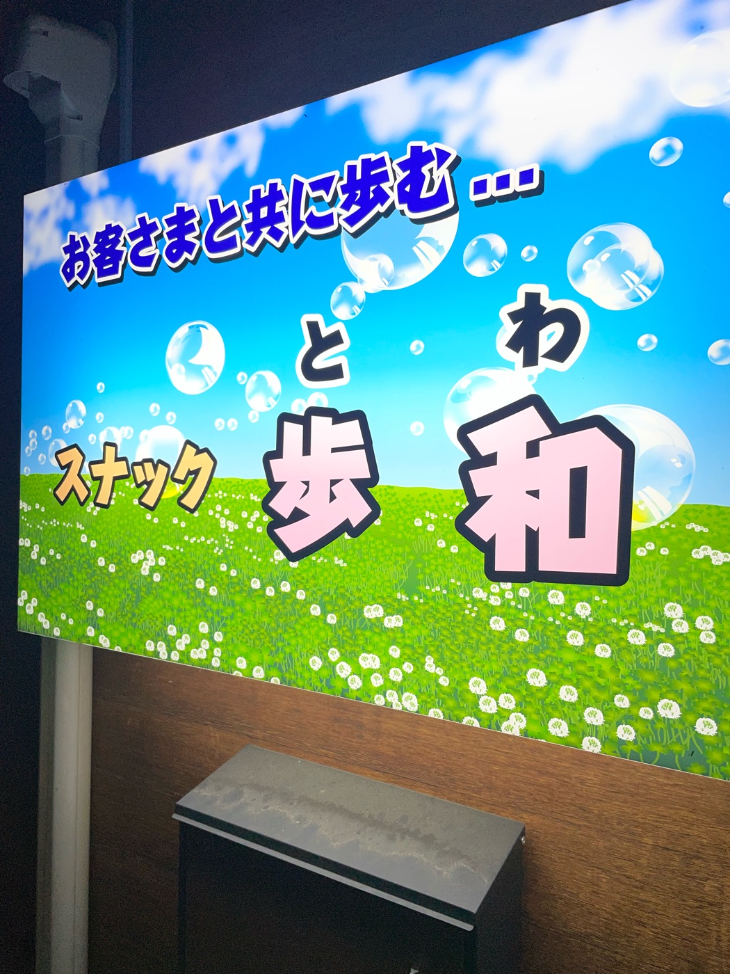「お客さまと共に歩む… スナック歩和」と書かれた青空と草原の看板